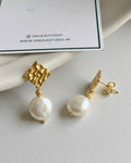 Pearl earrings with gold accents on a white surface, featuring Anuka Studio branding.