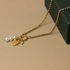 Gold necklace with heart and pearl charms on a beige surface