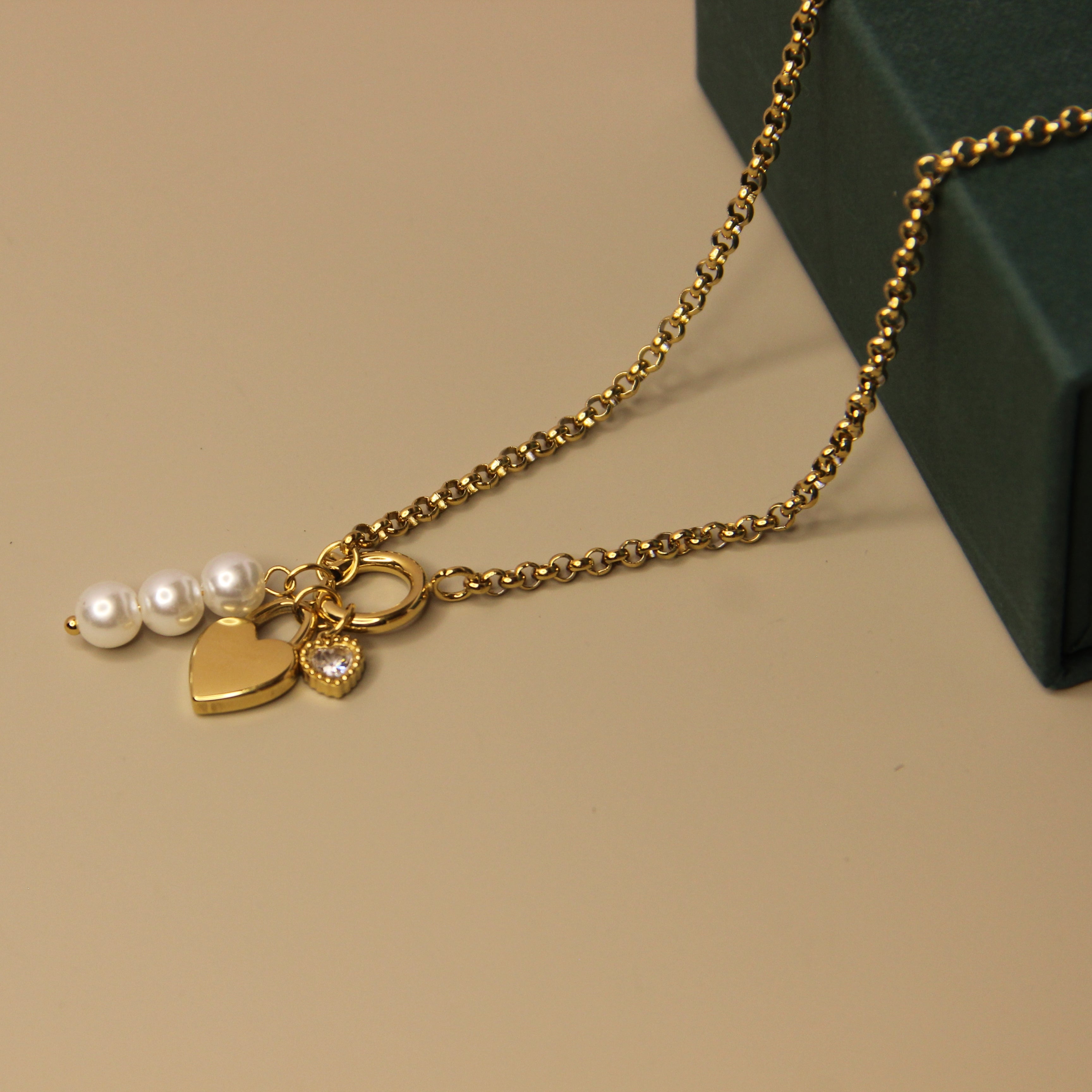 Gold necklace with heart and pearl charms on a beige surface