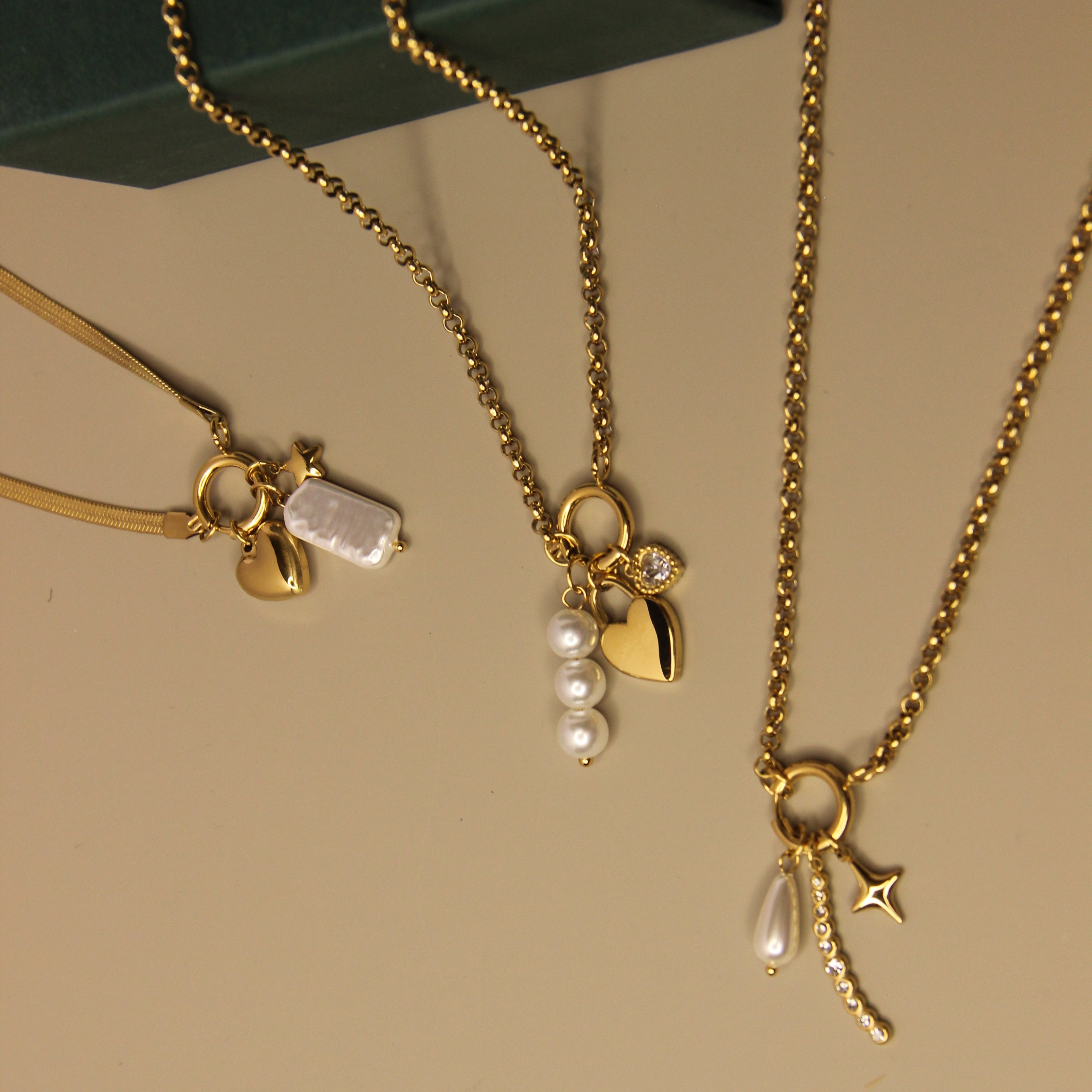 Gold necklaces with charms on a beige surface