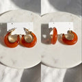 Pair of orange hoop earrings on a white card against a marble bacground